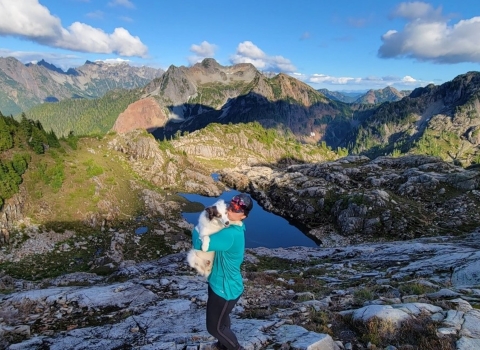 A woman holds a white dog with majestic mountains in the background