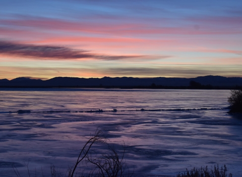 Early sunrise colors over a lake, with dark mountains in the distance