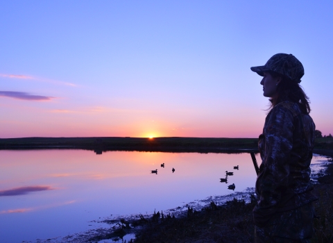 person waterfowl hunting by a wetland at sunrise