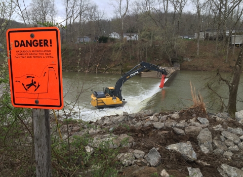 Crane removing dam with danger sign in the foreground