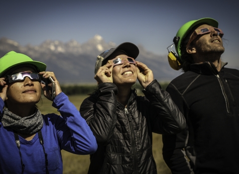 Three people wearing special eclipse glasses, stare up