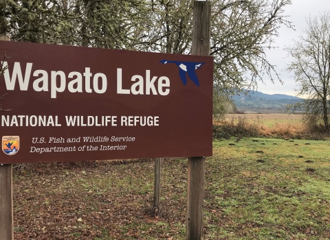 Picture of the Wapato Lake National Wildlife Refuge sign. The refuge is in the background.