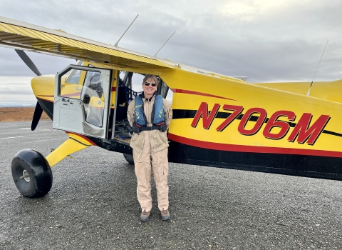 Kara Hilwig standing next to a single engine bush plane on a dirt airstrip. 