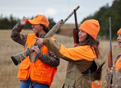 three women wearing orange stand together with long guns