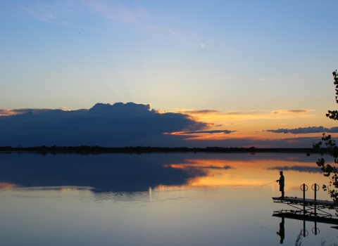 Silhouette of a man fishing as the sun sets over the water.