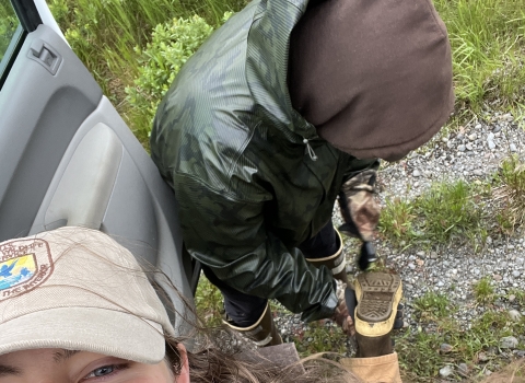 Biologist smiling while lifting a boot up to have friend clean dirt out of tread. 