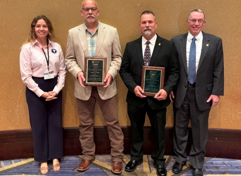 4 people pose; middle 2 with plaques