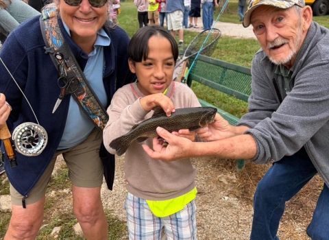 Child posing with volunteers holding fish