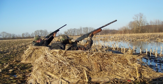 Two hunter with shotgun raised from camouflage dirt mounds. 