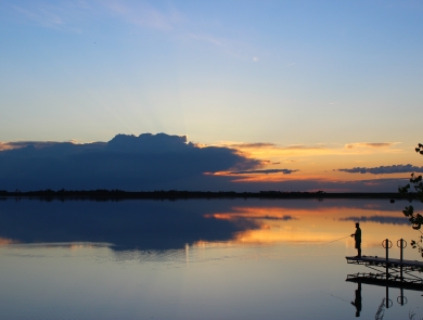 Silhouette of a man fishing as the sun sets over the water.
