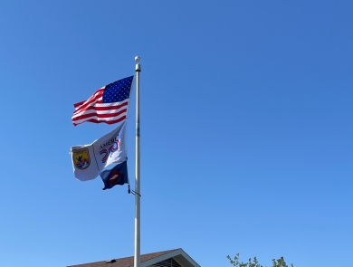 3 flags on flagpole with US flag atop USFWS ones. Building behind flagpole reads Garrison Dam National Fish Hatchery